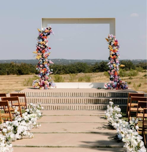 Outdoor ceremony with a flower-covered arch and a flower-lined aisle