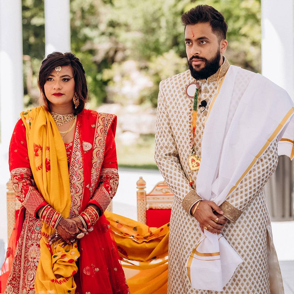 Bride in red and gold and groom in embroidered ivory at their wedding ceremony