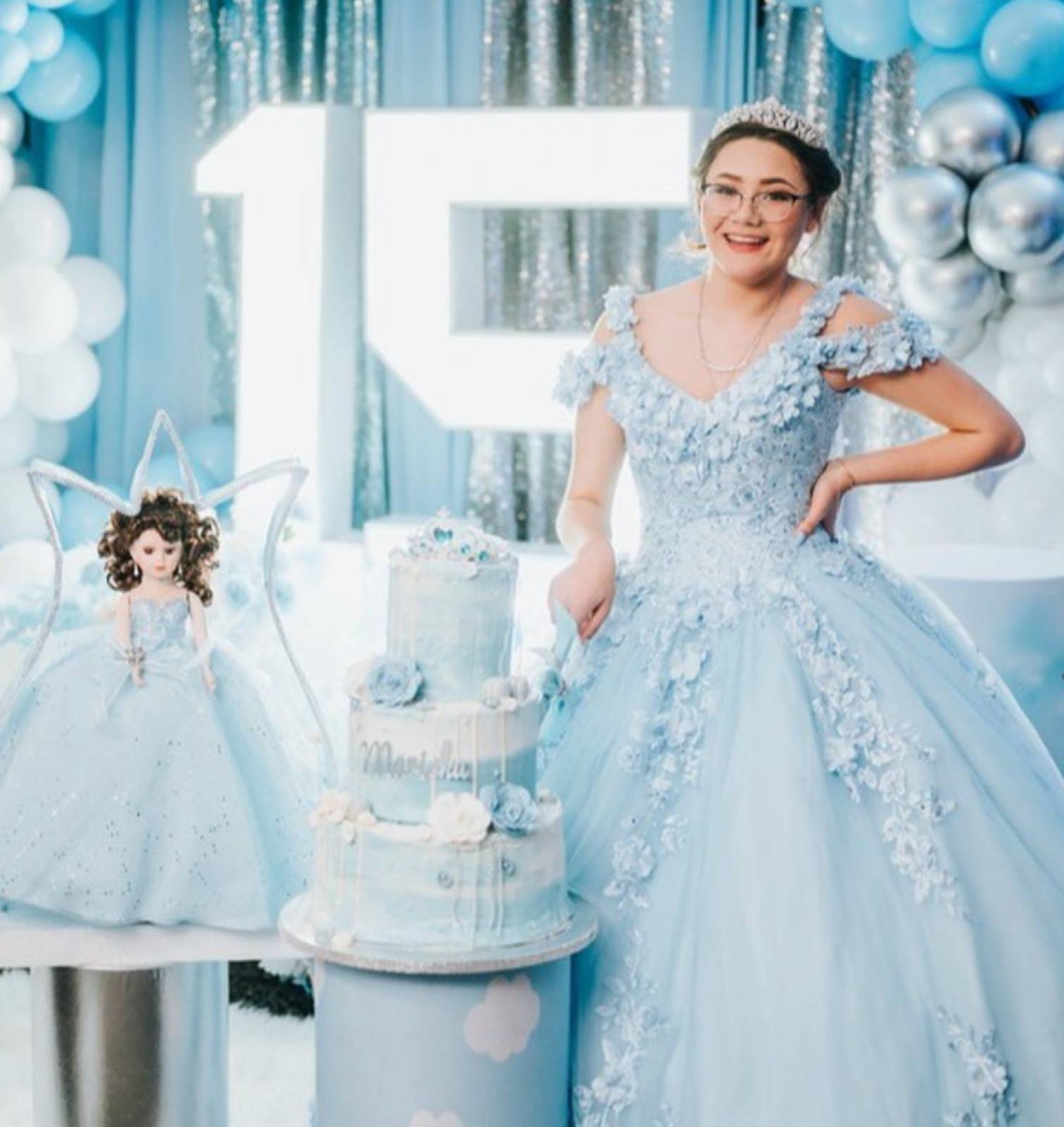 Young woman in a blue quinceañera gown and tiara beside her cake