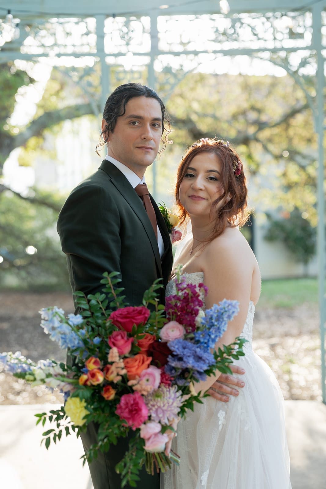 Bride holding a bouquet of pink, blue and orange flowers beside the groom