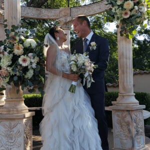 Laura and Steve under a floral arch between stone columns