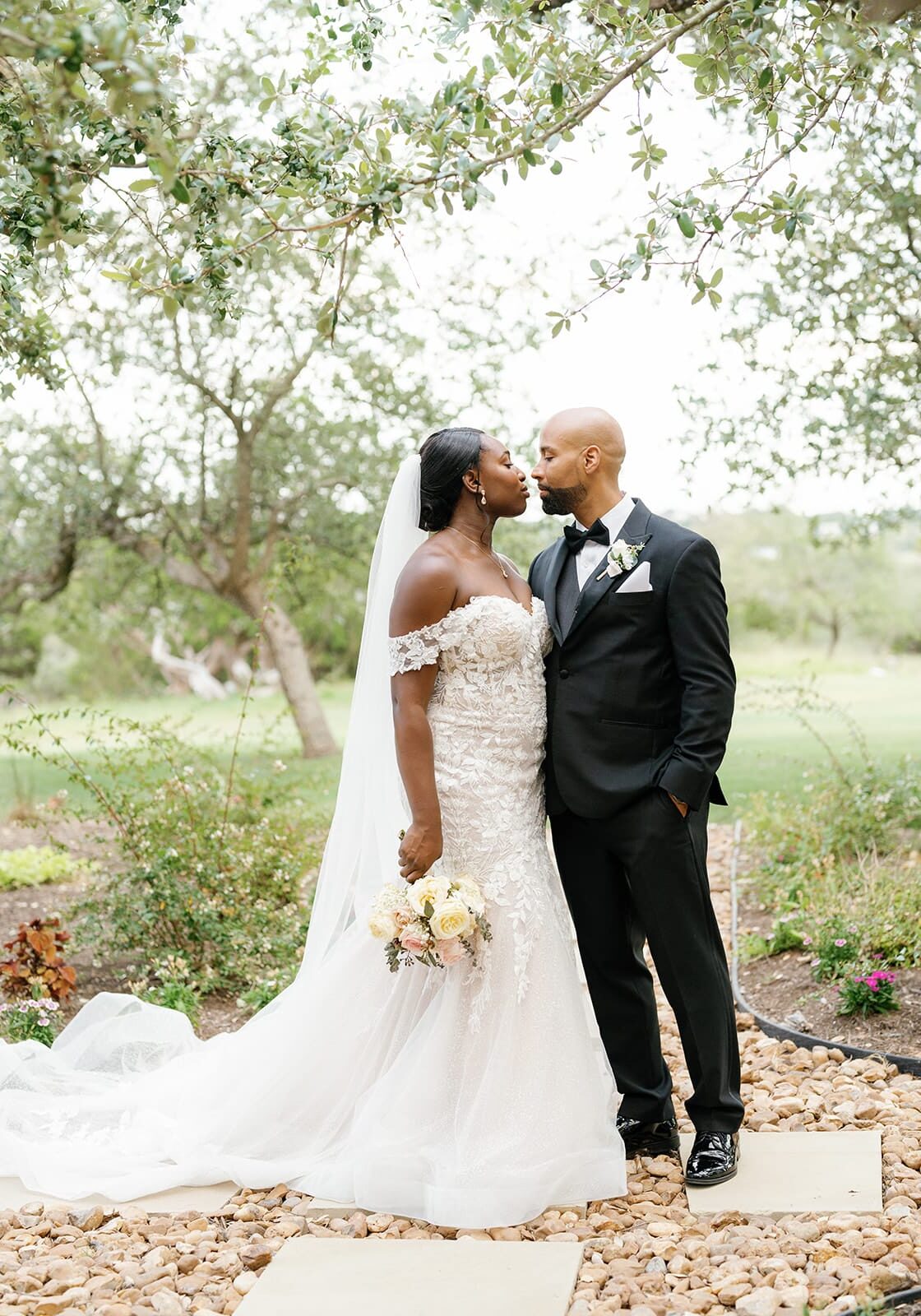 Bride and groom kissing on a garden path under oak trees