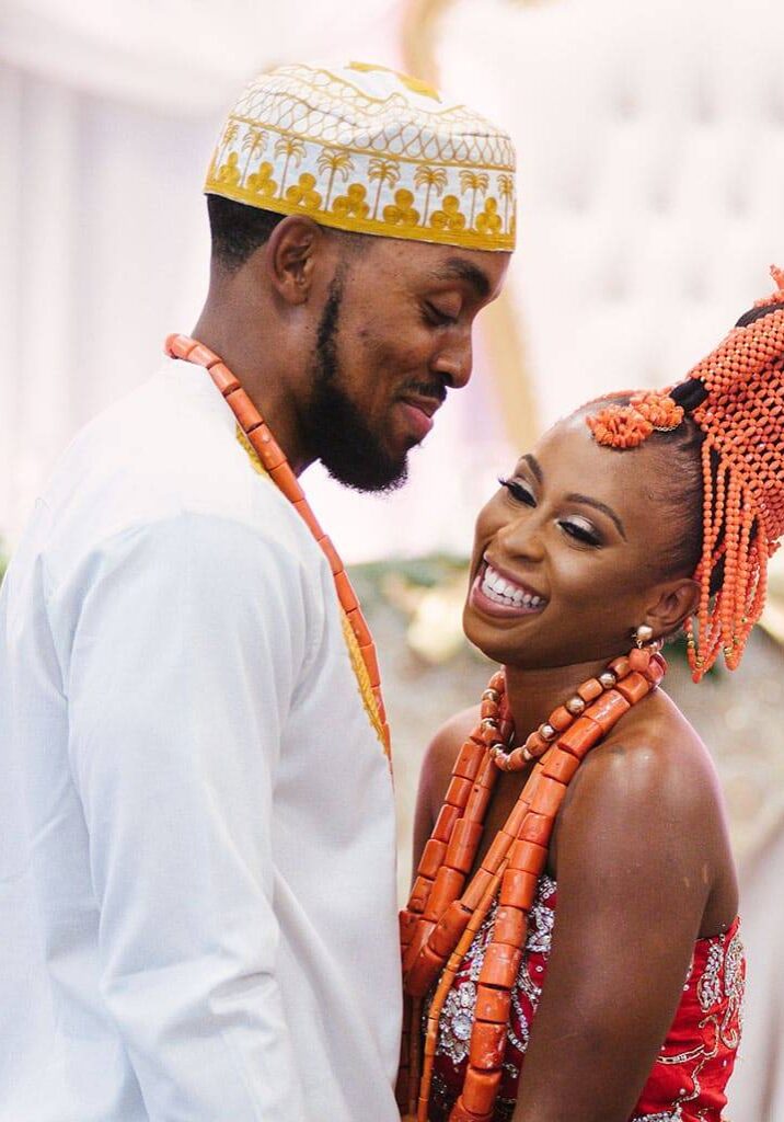 Bride and groom in coral beads and traditional wedding attire, smiling at each other